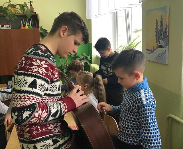 студент групи ММ-12 Володимир Решетнік дає учням можливість пробувати пограти на гітарі